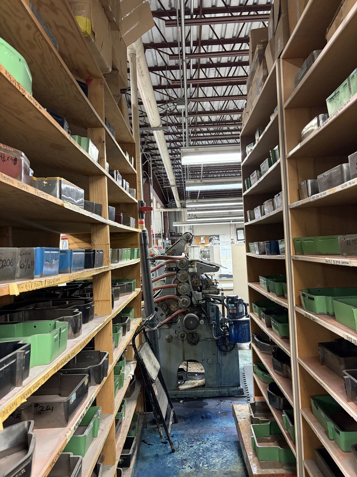 Aisles of wooden racks holding hundreds of envelope cutting dies, with a vintage envelope machine at the end of the row.