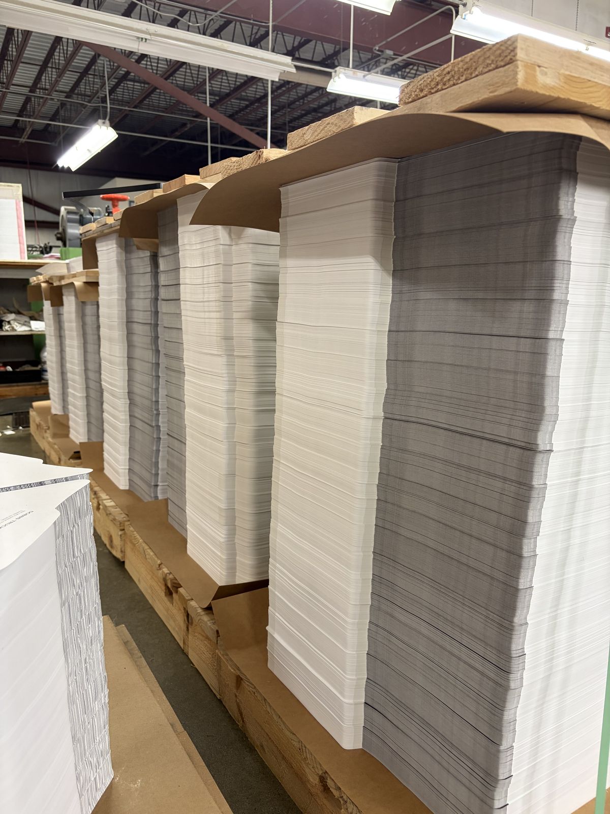 Tall stacks of printed flat stock jogged and lined up on pallets, waiting to be cut.