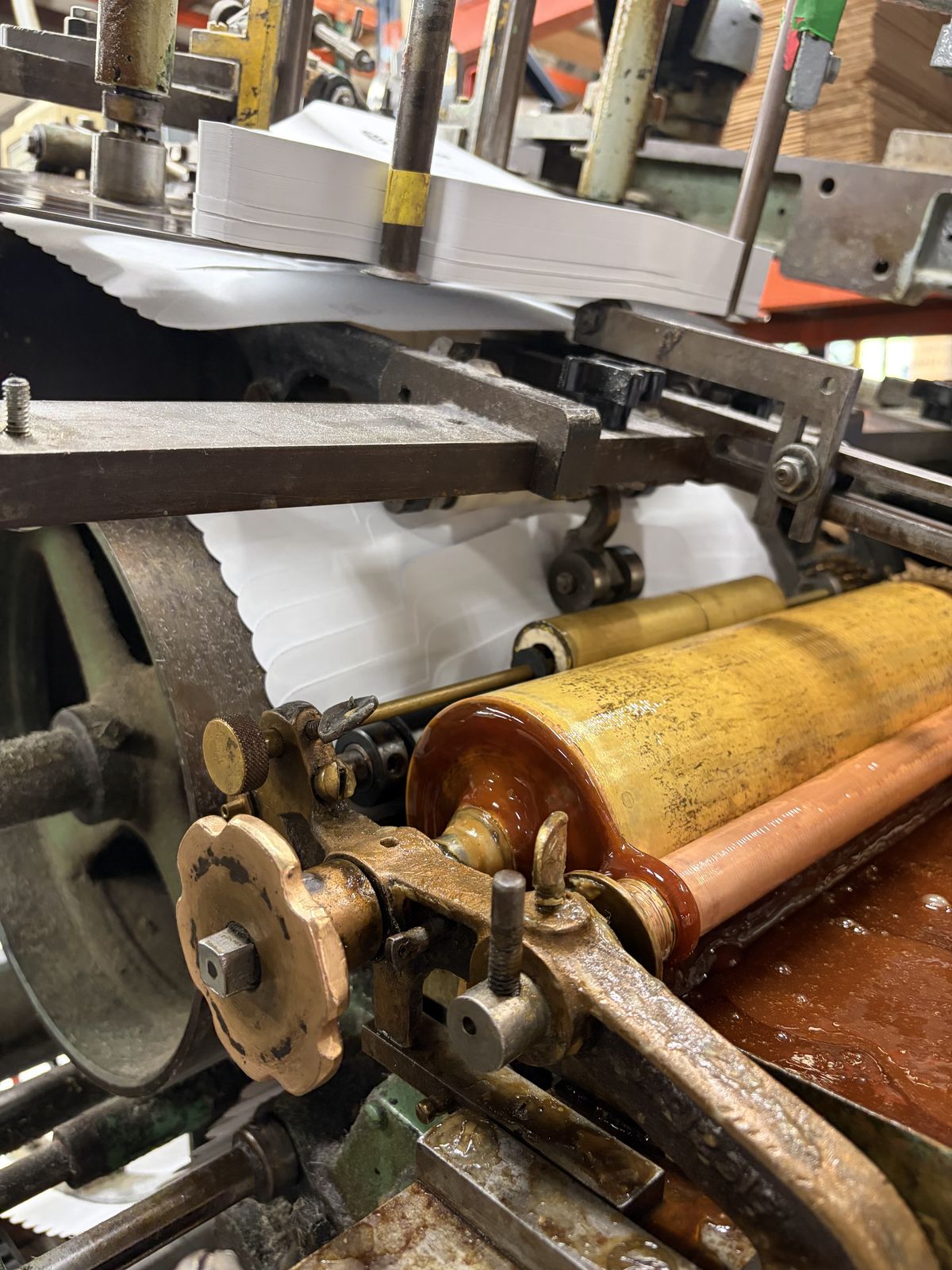 Amber glue coating the rollers of an envelope folding machine mid-run.