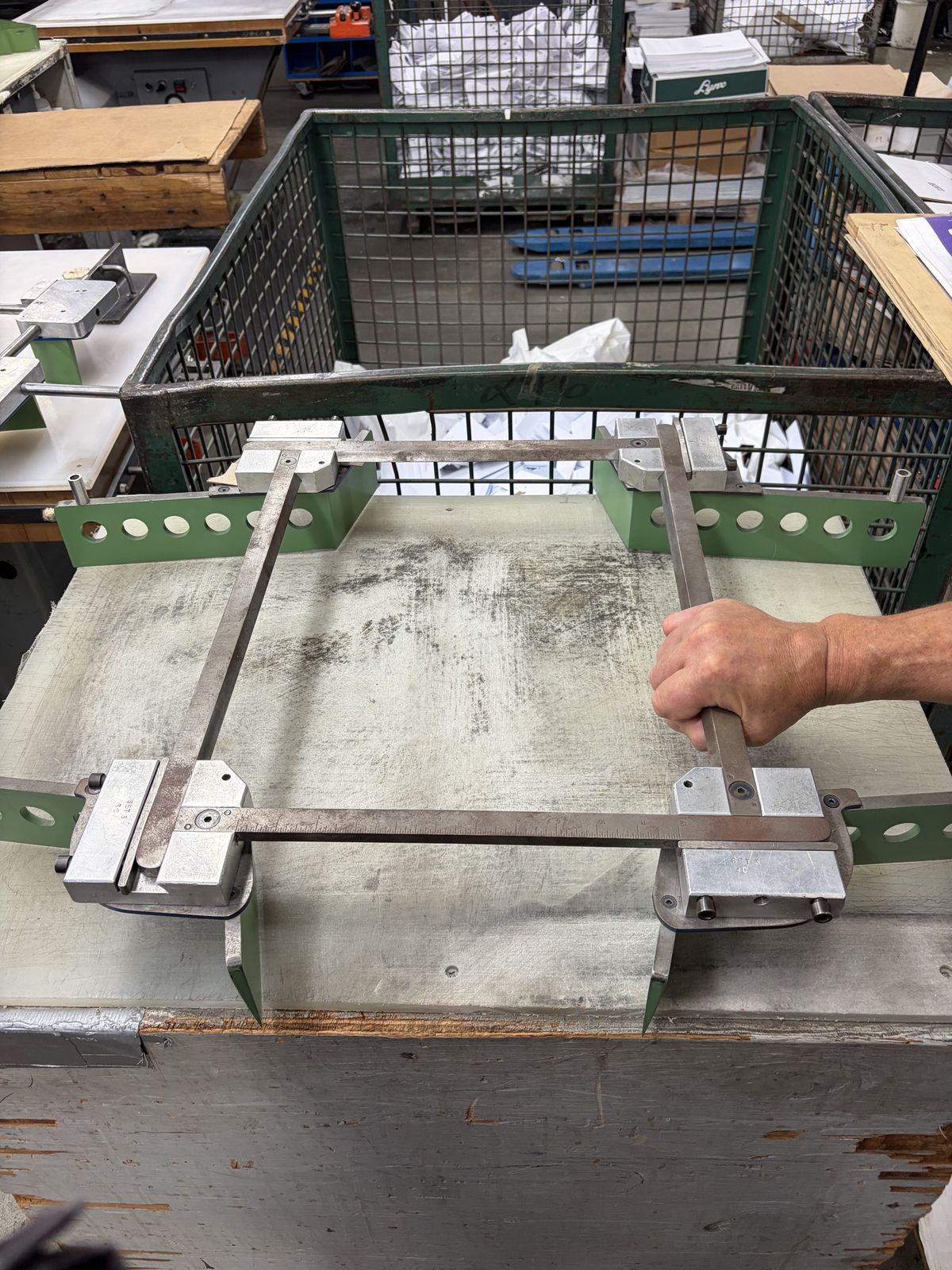 A hand lifting a large adjustable spider die from a workbench.