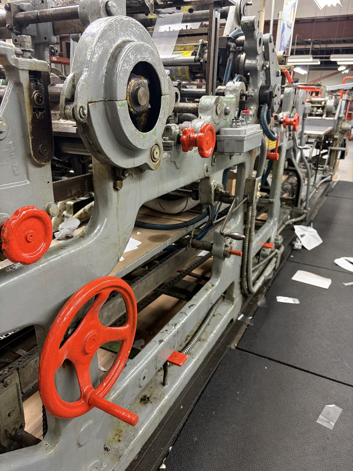 Rows of orange handwheels and dials along the frame of a wide range envelope converting machine.