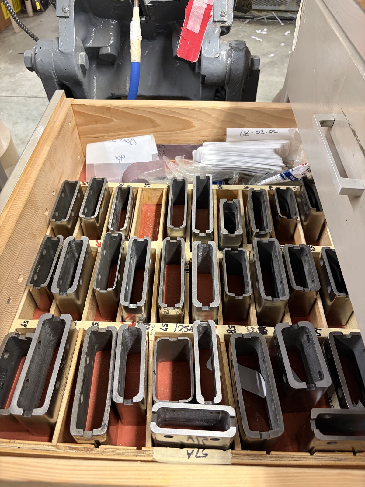 A wooden drawer holding dozens of labeled window punches in different sizes.